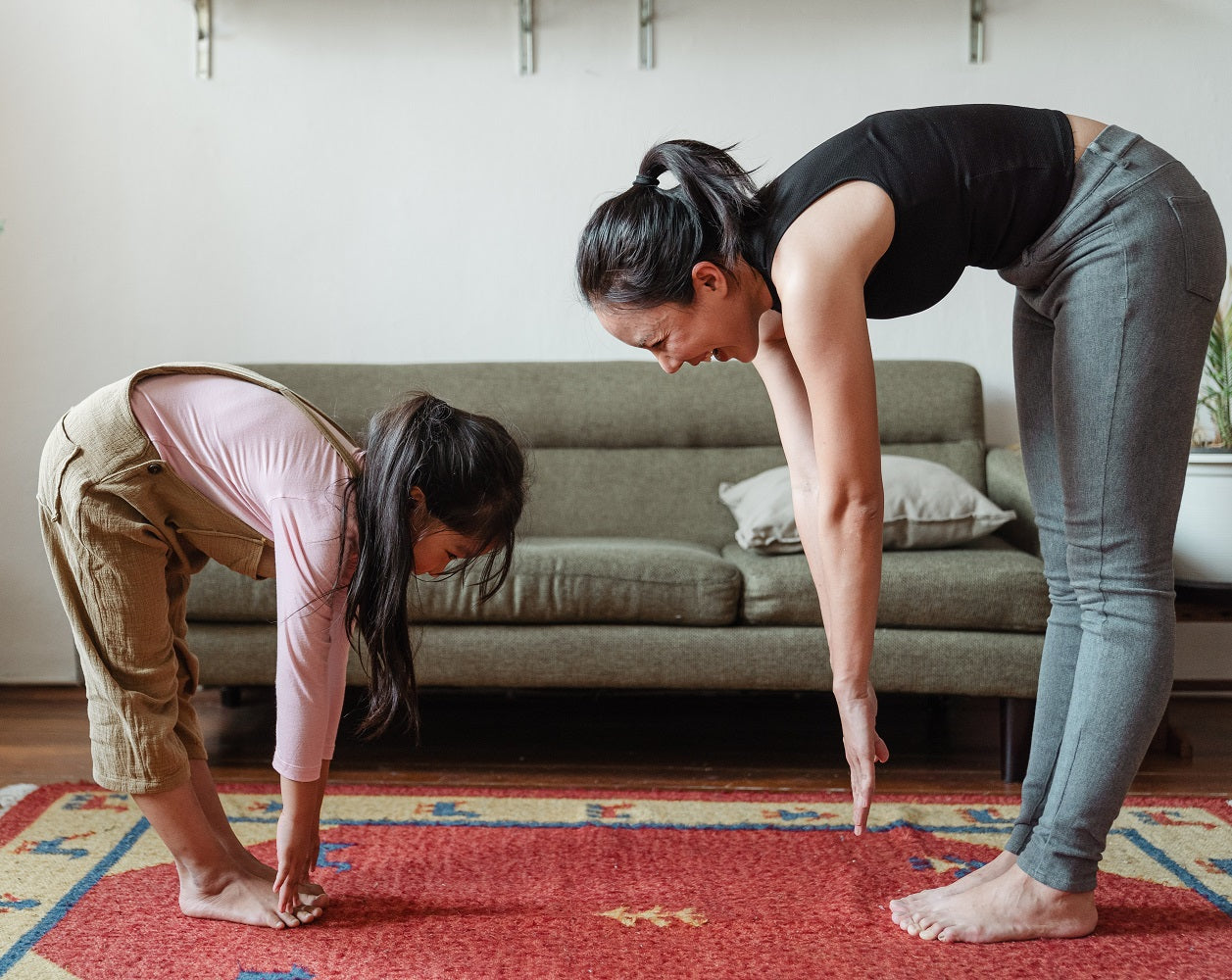Mother with daughter stretching on the carpet in the living room next to the sofa