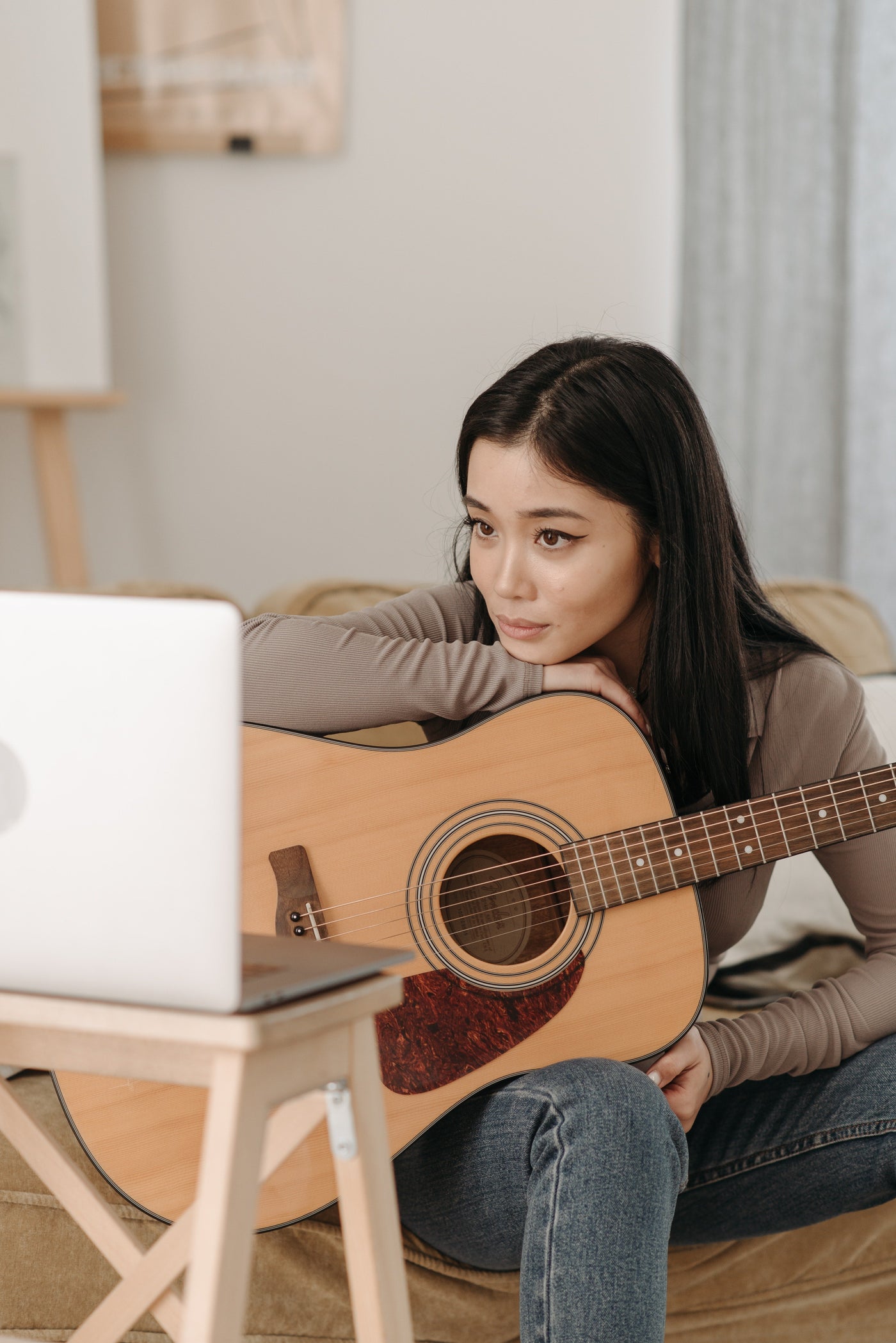 The young asian women holding the guitar and wathing on the laptop